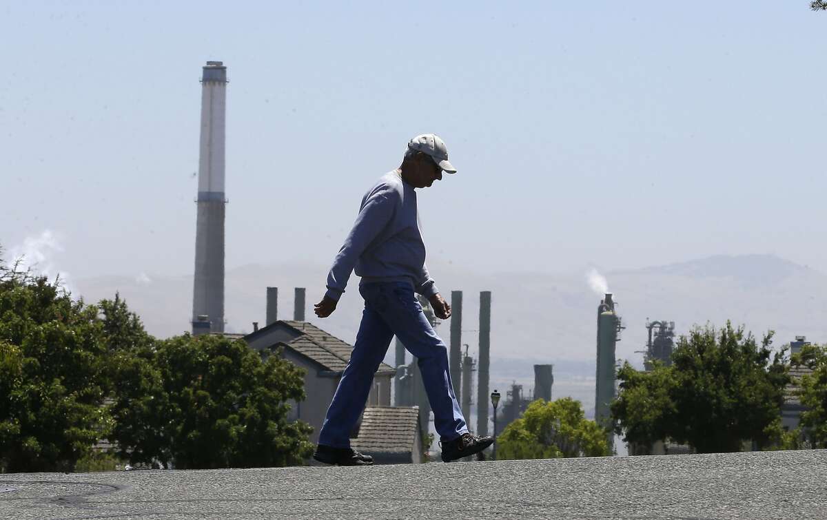 File- In this July 12, 2017 file photo the stacks from the Valero Benicia Refinery are seen as a pedestrian walks in a nearby neighborhood, in Benicia, Calif. Gov. Jerry Brown and state lawmakers got national attention last month for extending the state's "cap and trade" climate change law that keeps alive a program that raises hundreds of millions of dollars a year by auctioning off permits to release climate-changing gases. California lawmakers return Monday, Aug. 21 , from a monthlong break with a busy agenda that includes tackling the state's housing crisis and deciding whether to make California a statewide sanctuary for people living illegally in the U.S. (AP Photo/Rich Pedroncelli, file)