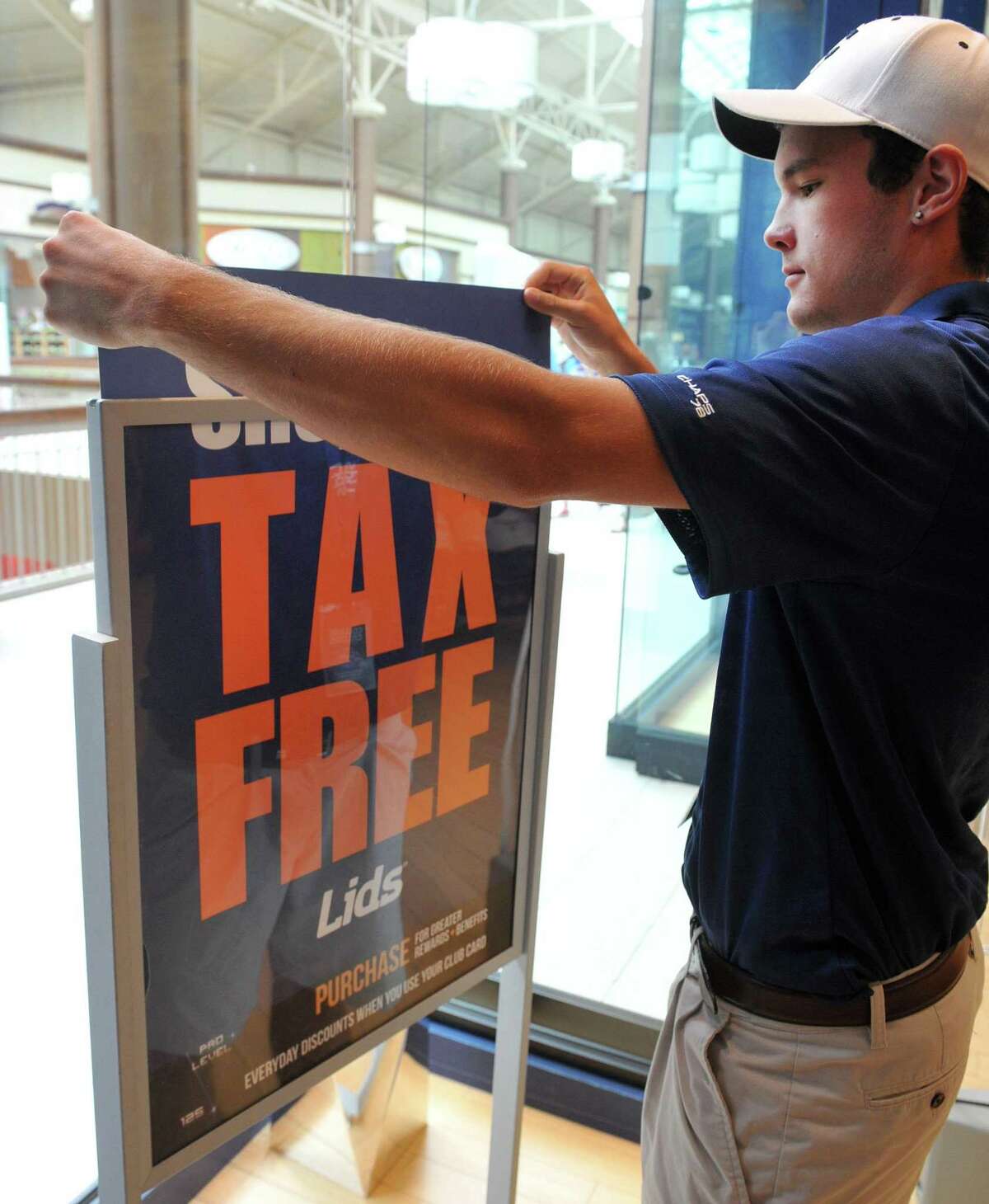 A worker places a display in the window of Lids at the Danbury Fair mall on the first day of tax free week in 2013.