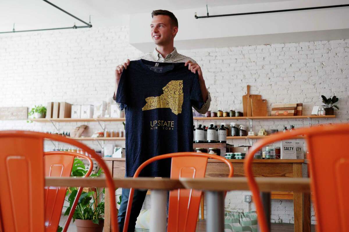 Schuyler Bull, owner of the Fort Orange General Store, holds up one of the t-shirts sold at his store on Monday, Sept. 11, 2017, in Albany, N.Y. The t-shirt is designed by MW Neighborhoods. (Paul Buckowski / Times Union)