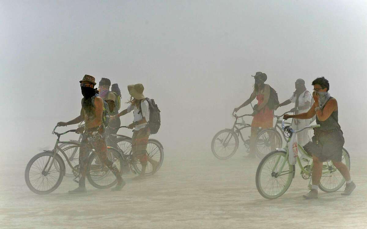FILE PHOTO: Burning Man participants walk their bikes during a dust storm at the annual Burning Man event on the Black Rock Desert of Gerlach, Nev., on Friday, Aug. 29, 2014. Organizers call Burning Man the largest outdoor arts festival in North America, with its drum circles, decorated art cars, guerrilla theatrics and colorful theme camps. 
