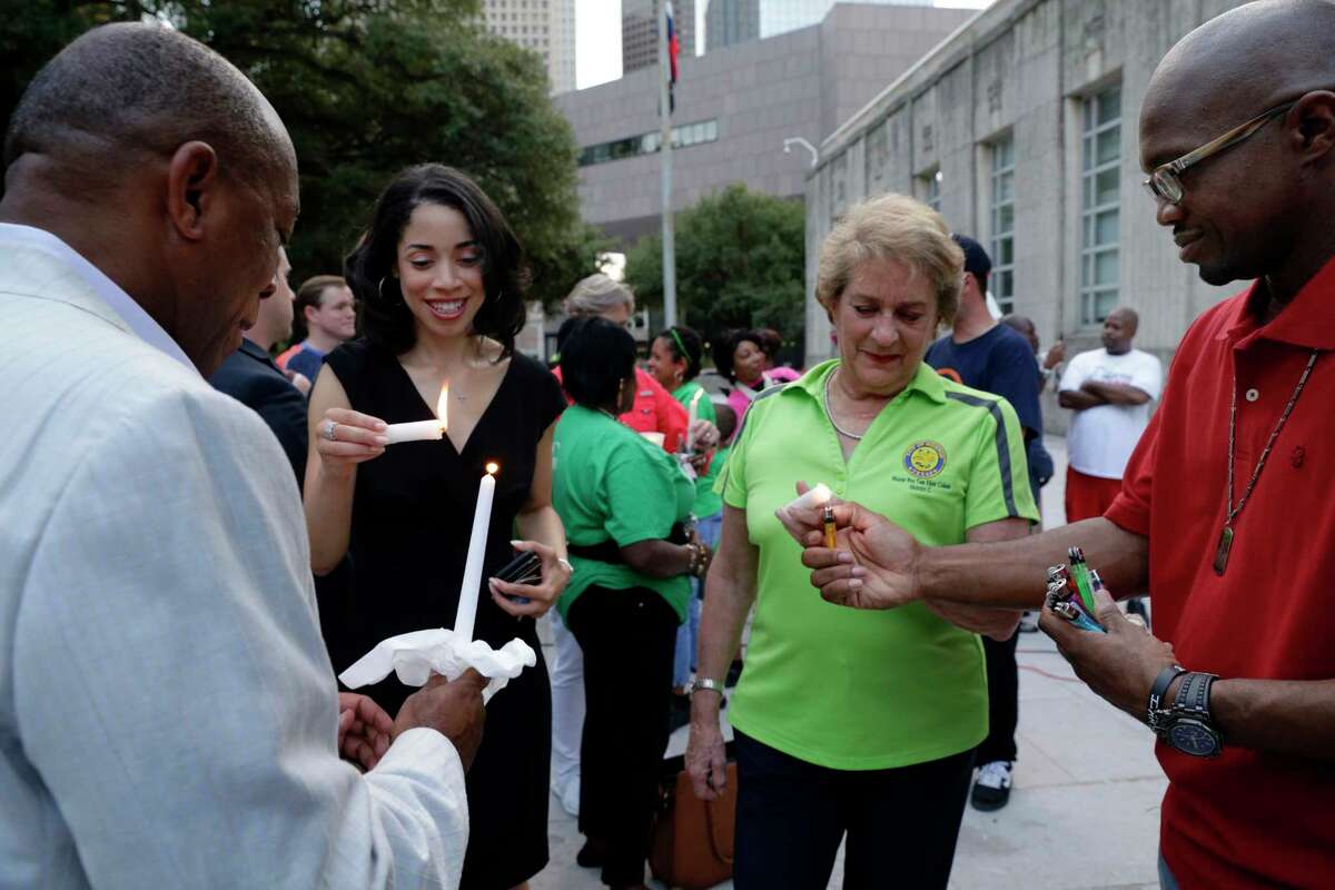 From left, Mayor Sylvester Turner, Amanda Edwards and Mayor Pro Tem Ellen Cohen get their candles lit by pastor V. Eric Gordon during a candlelight ceremony on the steps of City Hall Sunday night.