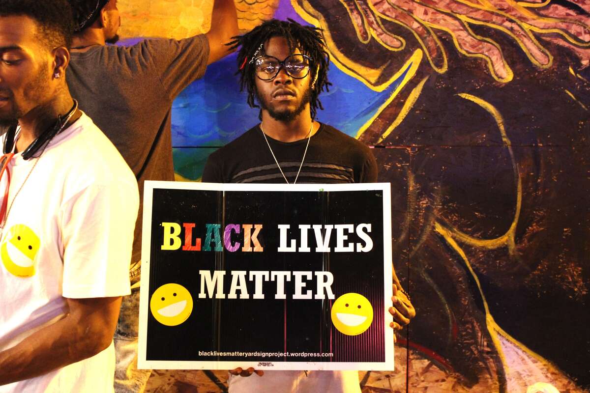 Donovan Meeks, of St. Louis, holds a 'Black Lives Matter' sign in front of a storefront on Delmar Blvd. in St. Louis. Citizens were gathered with art supplies in hand, painting over the pieces of wood in place of damaged storefront windows Monday evening.