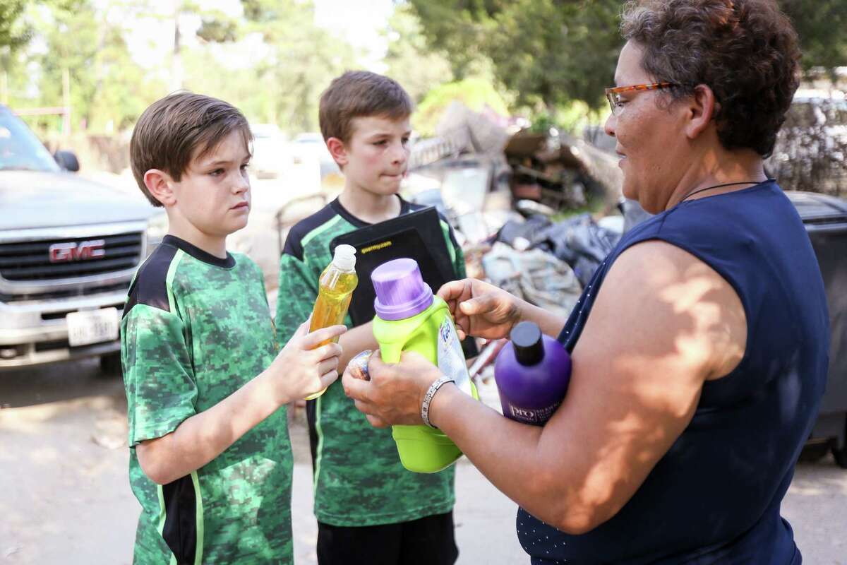 From the left, Boy Scouts Rafe and Jarrett Kotalik give cleaning supplies to Maria Sanchez, a resident who's home on River Oaks Drive was damaged in Hurricane Harvey, on Sunday, Sept. 17, 2017.