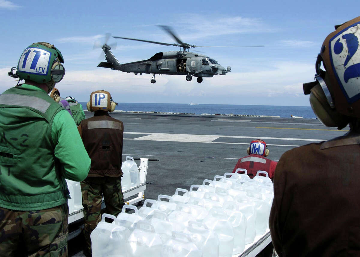 Sailors stand-by to load jugs of purified water into an approaching SH-60B Seahawk, assigned to the "Saberhawks" of Helicopter Anti-Submarine Squadron Light Four Seven (HSL-47), on the flight deck aboard the aircraft carrier USS Abraham Lincoln (CVN 72), January 11, 2005. Helicopters assigned to Carrier Air Wing Two (CVW-2) and Sailors from USS Abraham Lincoln (CVN 72) are supporting Operation Unified Assistance, the humanitarian operation effort in the wake of the Tsunami that struck South East Asia. The Abraham Lincoln Carrier Strike Group is currently operating in the Indian Ocean off the waters of Indonesia and Thailand. Picture taken January 11, 2005. REUTERS/U.S. Navy/Tyler J. Clements-Handout EDITORIAL USE ONLY