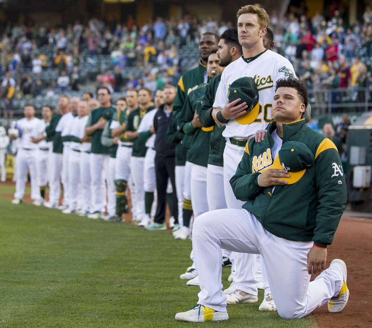 From right: Oakland Athletics catcher Bruce Maxwell (13) takes a knee as Oakland Athletics left fielder Mark Canha (20) puts his hand on his shoulder during the playing of the national anthem before an MLB baseball game between the Oakland Athletics and Texas Rangers at the Oakland Coliseum on Saturday, Sept. 23, 2017, in Oakland, Calif.