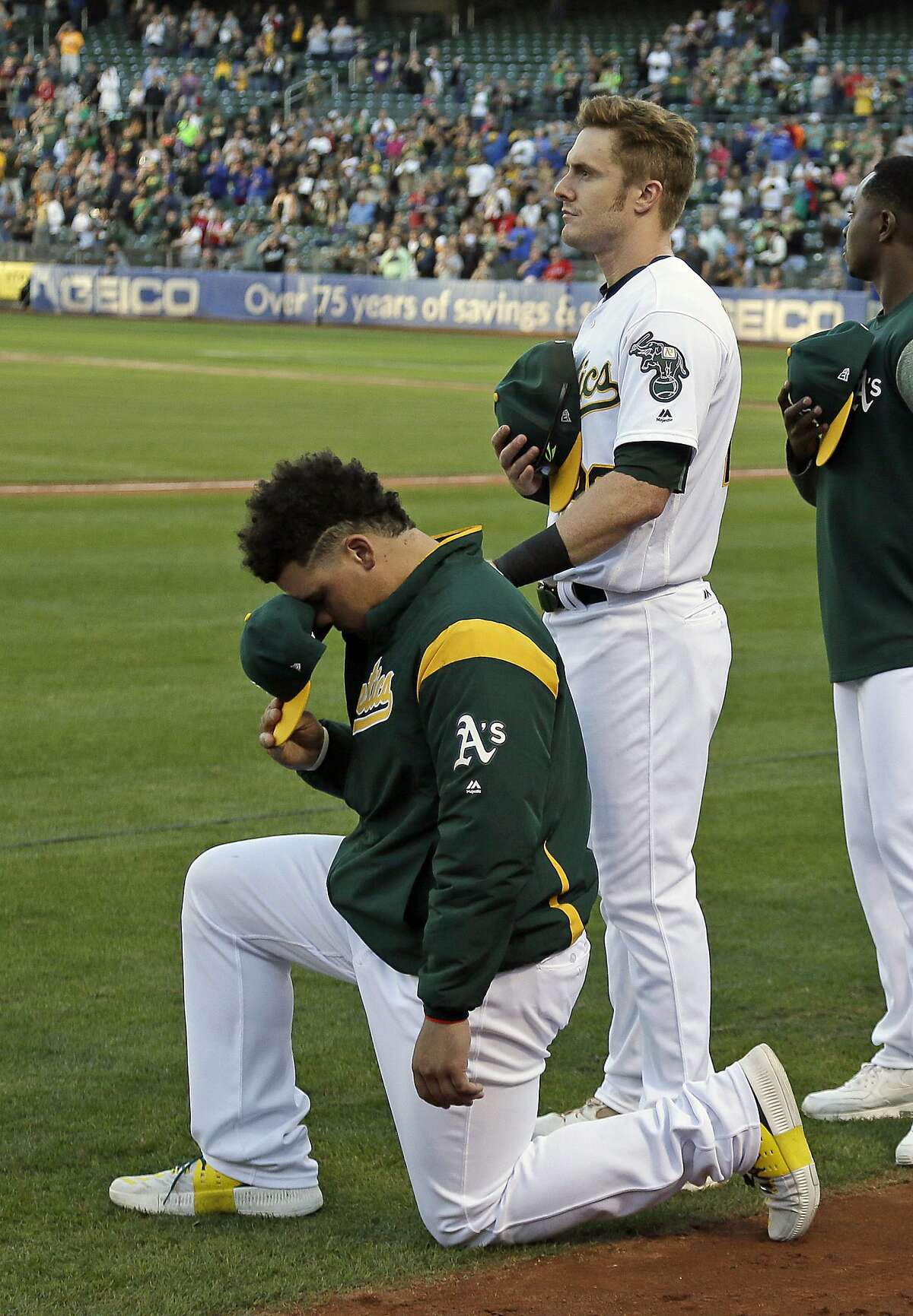 Oakland Athletics catcher Bruce Maxwell, left, kneels as teammate Mark Canha, right, looks on during the National Anthem before the start of a baseball game against the Texas Rangers Saturday, Sept. 23, 2017, in Oakland, Calif. Bruce Maxwell of the Oakland Athletics has become the first major league baseball player to kneel during the national anthem. (AP Photo/Eric Risberg)