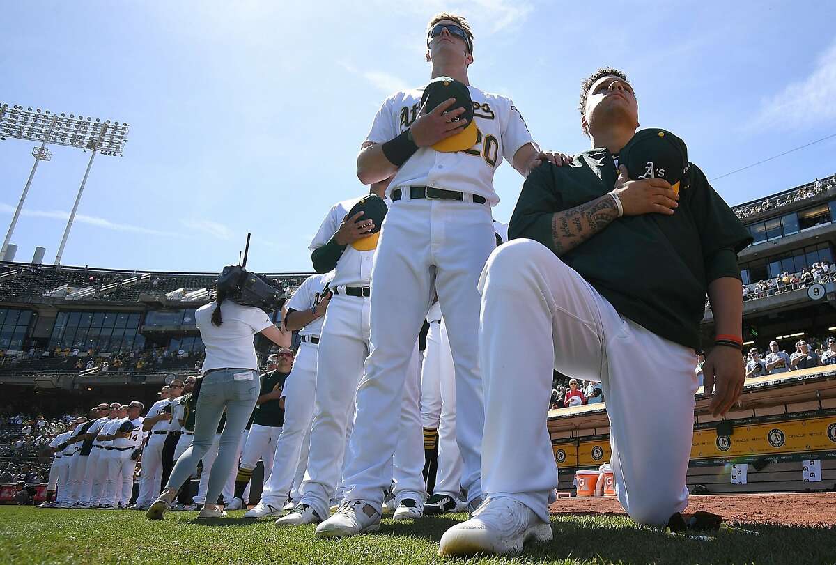 Bruce Maxwell of the Oakland Athletics kneels in protest next to teammate Mark Canha #20 duing the singing of the National Anthem prior to the start of the game against the Texas Rangers at Oakland Alameda Coliseum on September 24, 2017 in Oakland, California.