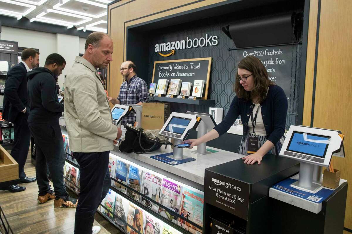 In this Thursday, May 25, 2017, photo, a salesperson helps a customer use his smartphone to make a payment at the Amazon Books store in the Time Warner Center at Columbus Circle, in New York. Amazon opened the retail store Thursday. Amazon, the e-commerce giant that changed how people shop for books, toilet paper and TVs, hit a new milestone Tuesday, May 30: Its stock topped $1,000 for the first time. (AP Photo/Mary Altaffer)