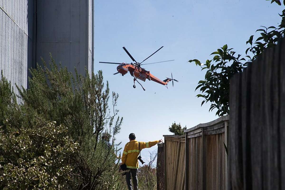 A helicopter drops water on an hillside of dry brush and grass as it threatened homes and caused evacuations on Tuesday, Sept. 26, 2017 in Oakland, Calif.