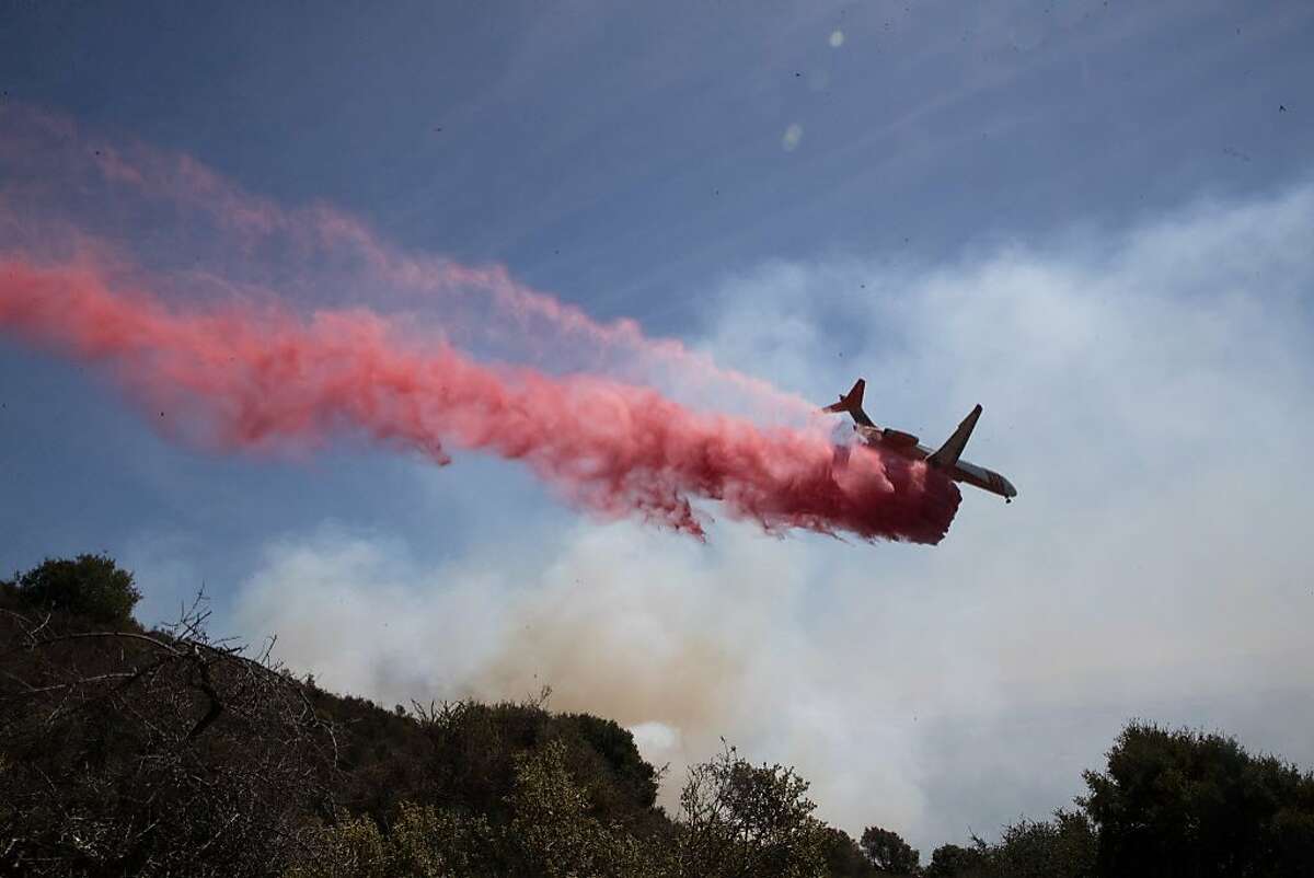 A jet plane drops fire retardent on a hillside fire of dry brush and grass as it threatened homes and caused evacuations on Tuesday, Sept. 26, 2017 in Oakland, Calif.
