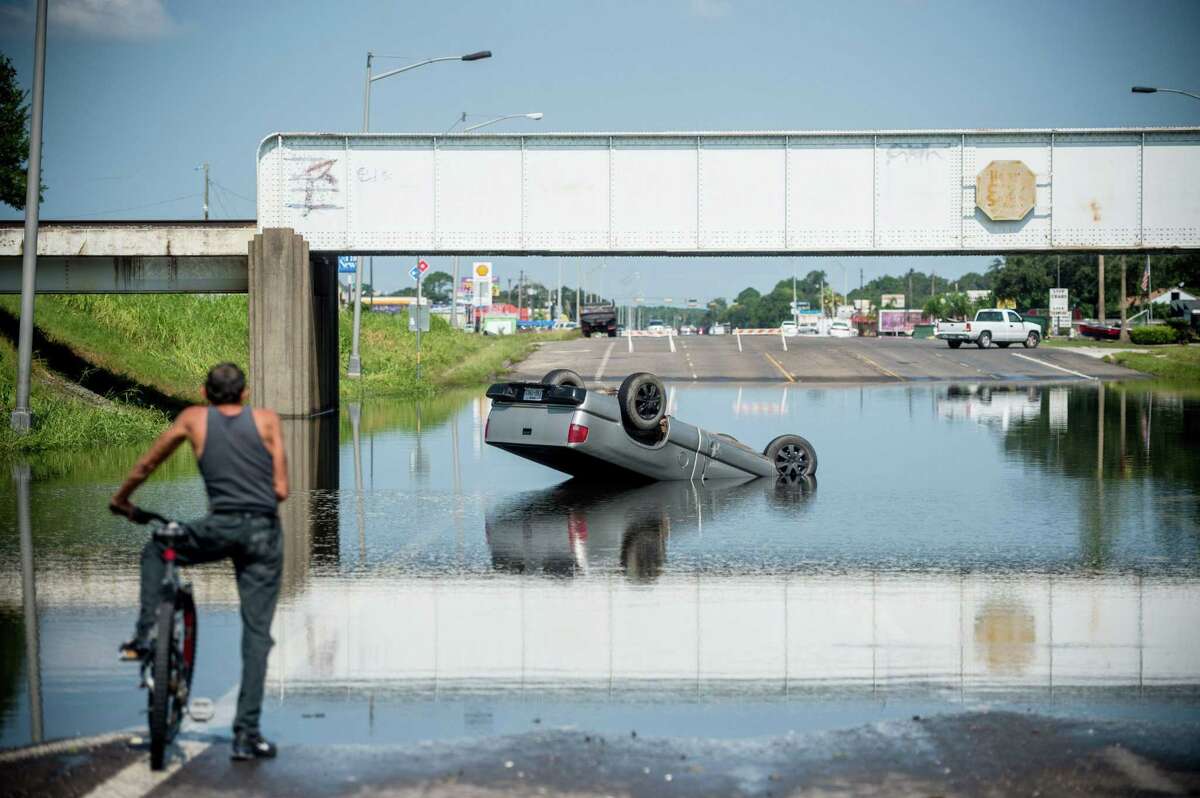 TOPSHOT - A bicyclist looks at a truck flipped into floodwater in Port Arthur, Texas on September 1, 2017. Houston was limping back to life on Friday one week after Hurricane Harvey slammed into America's fourth-largest city and left a trail of devastation across other parts of southeast Texas. As flood waters receded in Houston and residents began slowly returning home other nearby towns such as Rockport, Beaumont and Port Arthur were struggling to get back on their feet. / AFP PHOTO / Emily KaskEMILY KASK/AFP/Getty Images