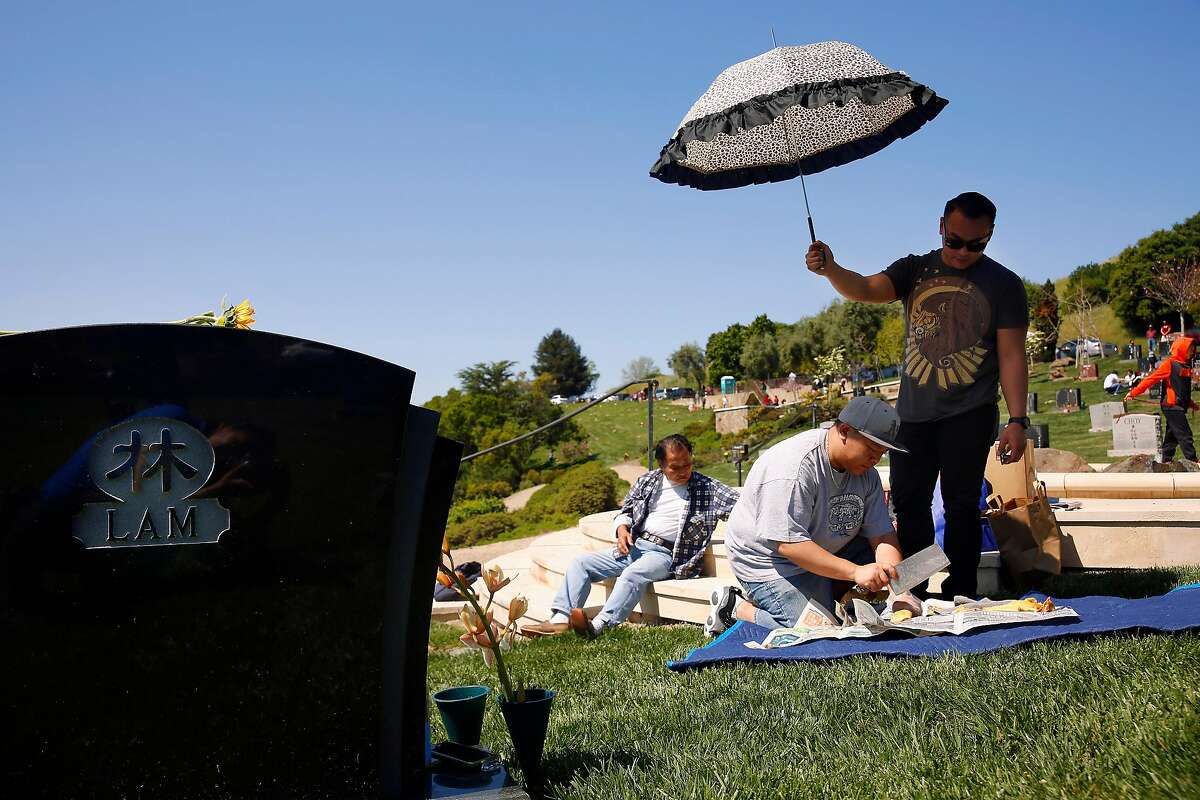 Eddie Lam (center), brother of Cecela Lam, slices a chicken to place at Cecelia Lam's gravesite as his brother Sunny Lam (right), brother of Cecelia Lam, shades him from the sun while Joseph Lam (left), father of Cecelia Lam, sits nearby as they pay their respects to Cecelia Lam as the family celebrates Ching Ming at Mountain View Cemetary on Sunday, April 2, 2017 in Oakland, Calif. Cecelia Lam was killed by her partner during a domestic violence incident in San Francisco in October of 2014,
