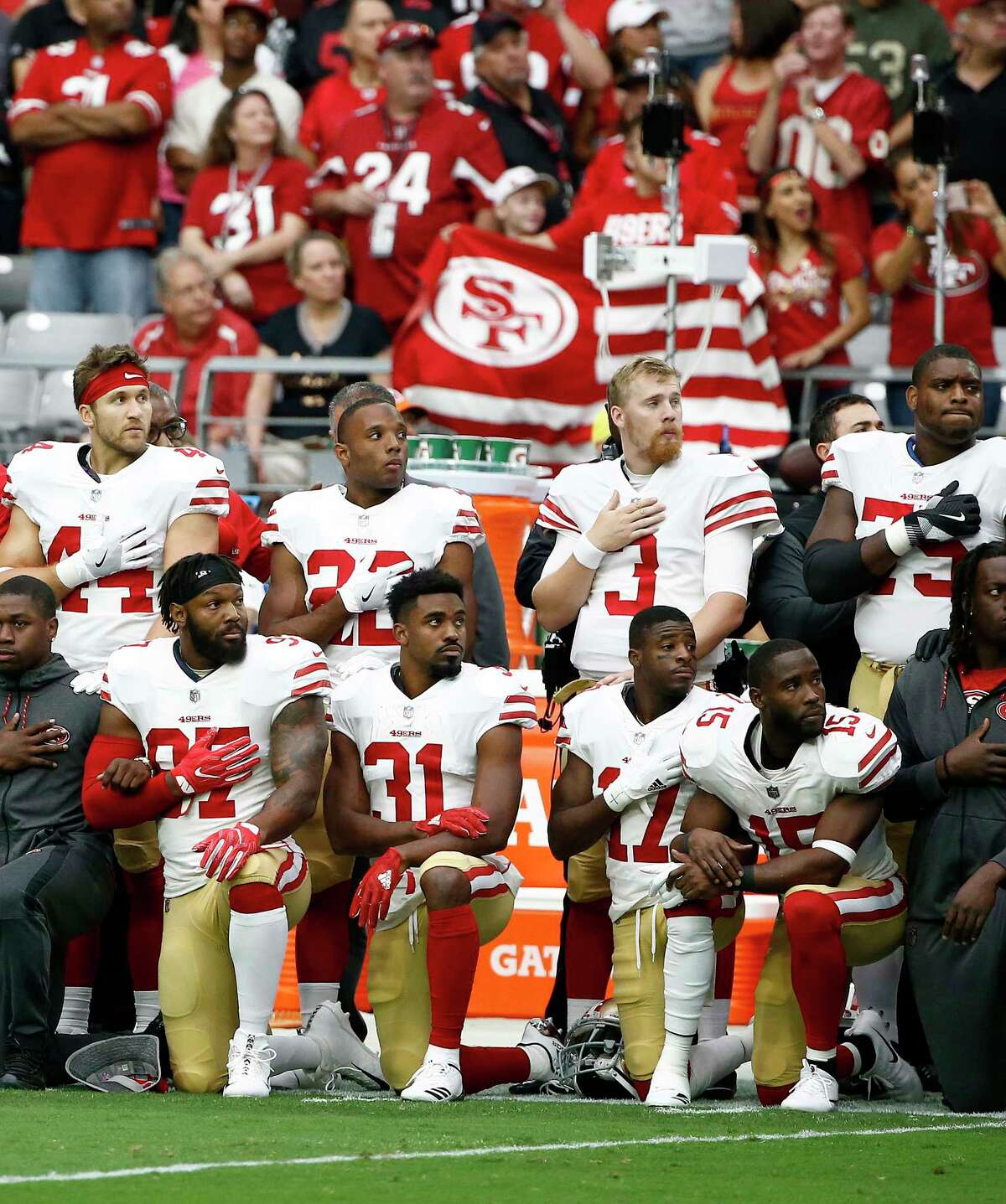 Some members of the San Francisco 49ers kneel as others stand during the national anthem prior to a game against the Cardinals in Glendale, Ariz.
