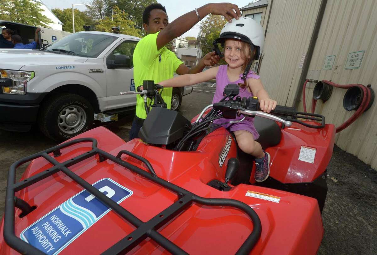 Norwalk Parking Authority employee Simon Zerufael helps Isla Depmsey, 5, of Wilton, at top, gets fitted with a helment while sitting on a quad during the Norwalk Fire, Police, and Public Works Departments and Norwalk EMS Open House and Touch- a- Truck Sept. 30 at the Public Works Center and fire training tower on South Smith Street in Norwalk. All four Departments featured hands-on activities, give-aways and demonstrations for all ages.