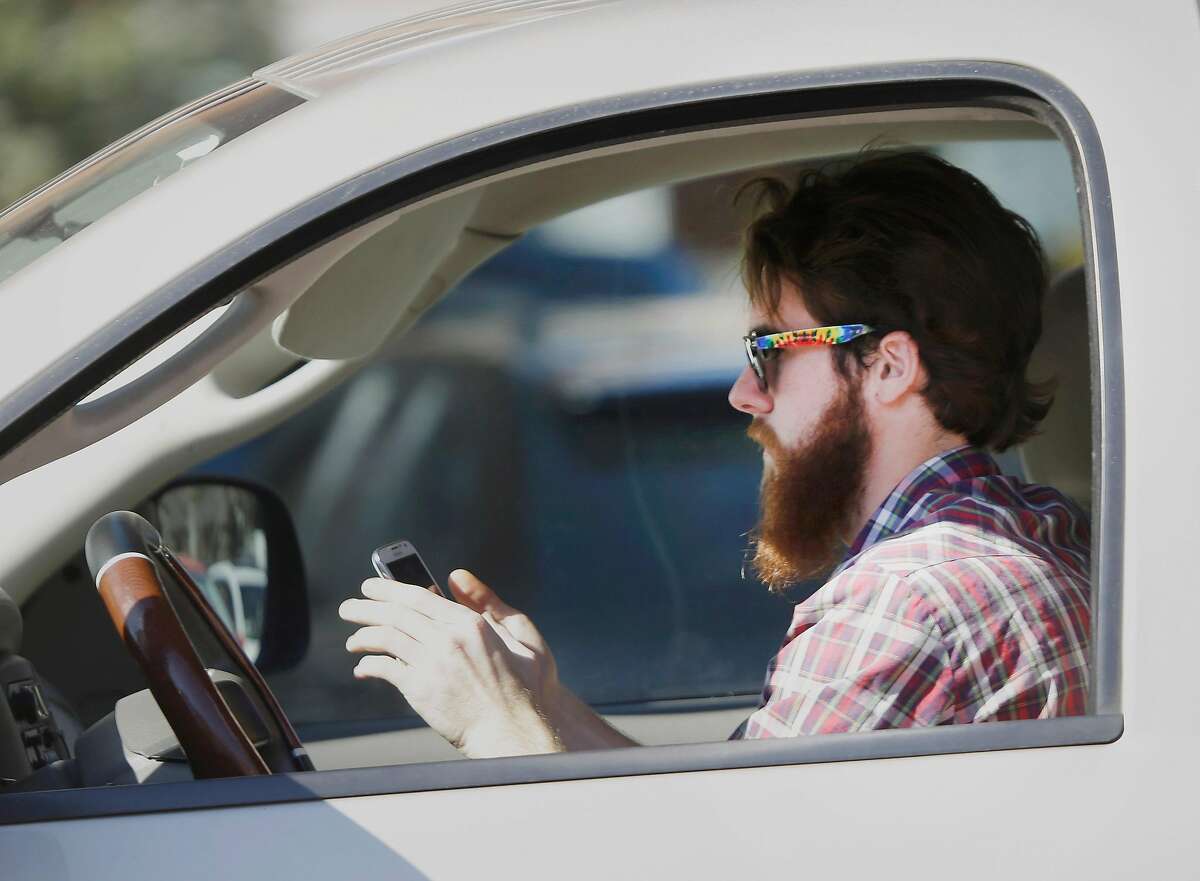 An man works his phone as he drives through traffic in Dallas, Tuesday, Feb. 26, 2013. Texas lawmakers are considering a statewide ban on texting while driving. (AP Photo/LM Otero)