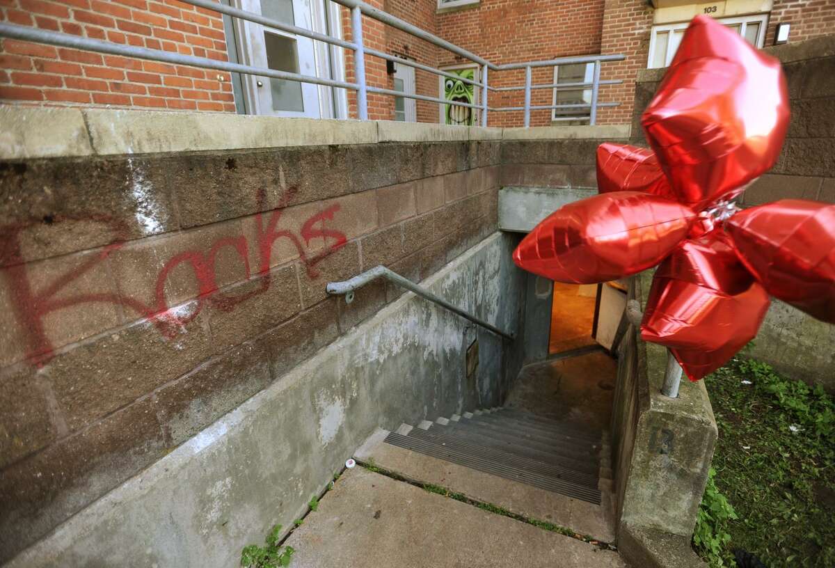 A stairway to the basement of Charles Greene Homes housing project Building No.1 is marked with the spray painted name "Racks", and a bunch of helium balloons where Jeri “Racks” Kollock, 18, was shot and killed on Wednesday. At left, Chickie Bush, of Bridgeport, stands outside the building.