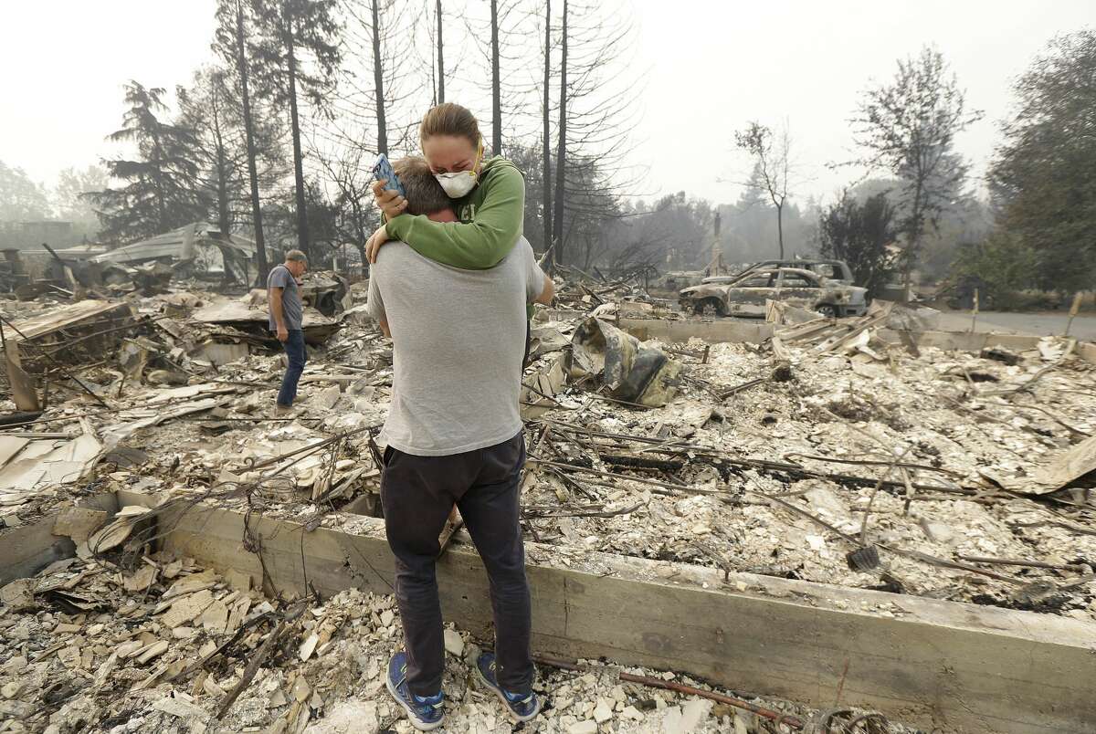 FILE - In this Oct. 10, 2017, file photo,Todd Caughey hugs his daughter Ella as they visit the site of their home destroyed by fires in Kenwood, Calif. For many residents in the path of one of California's deadliest blazes, talk is of wind direction, evacuations and goodbyes.