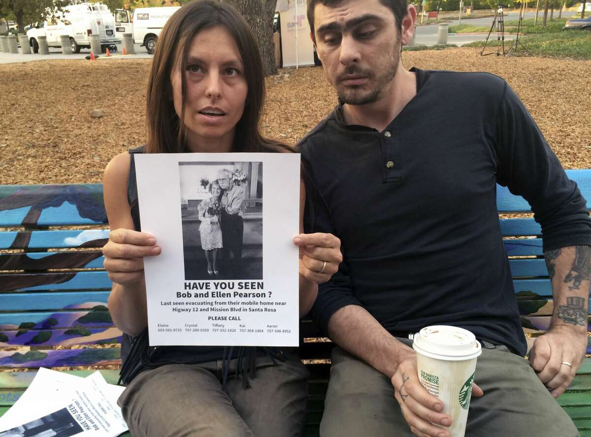 Chrystal Couto holds a poster of her grandmother as Aaron Austin looks on in Santa Rosa, Calif. on Friday, Oct. 13, 2017. The couple from Redway, are searching for Couto's grandmother and her husband, who haven't been heard from since a wildfire tore through the older couple's Santa Rosa neighborhood. They are hanging flyers in evacuation centers with photos of the older couple. (AP Photo/Paul Elias)
