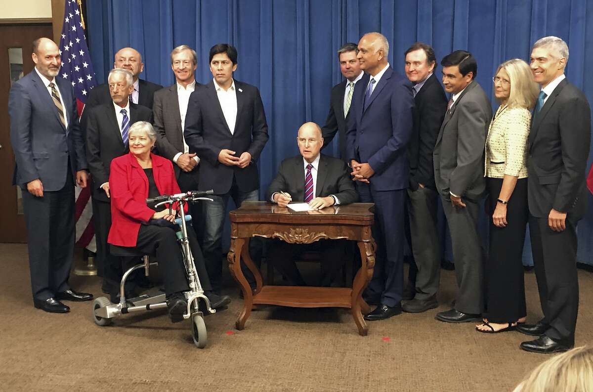 Gov. Jerry Brown, center, signs legislation by Democratic state Sen. Ed Hernandez (standing to Brown's left) to require drug makers to provide 60 days advance notice before dramatically raising drug prices in California at the Capitol in Sacramento Monday, Oct. 9, 2017. (AP Photo/Kathleen Ronayne)