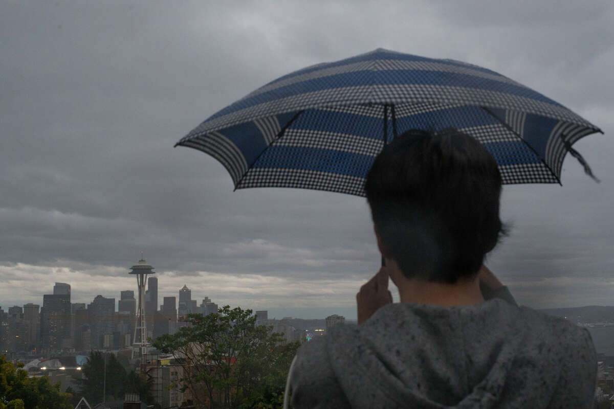 A spectator shields himself from the rain as he takes a photo of the Seattle skyline in the rain on Wednesday, Oct. 18, 2017.