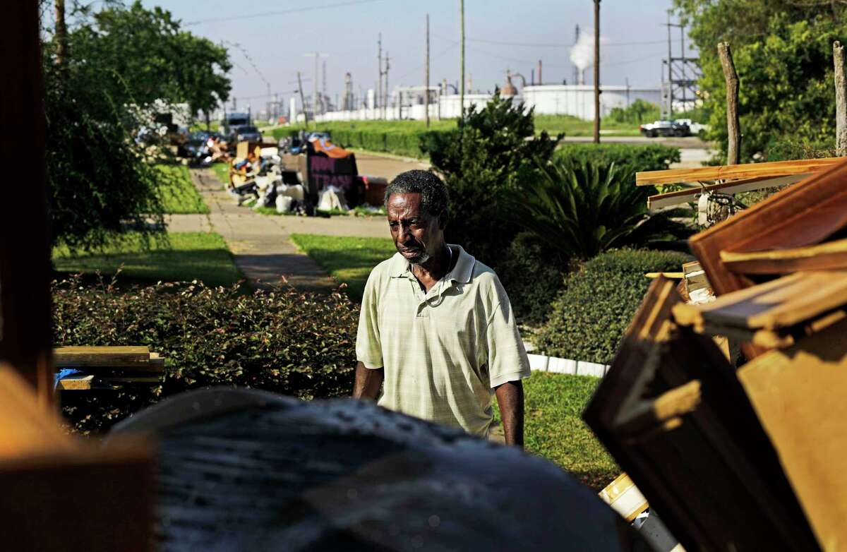 Samuel McGlory Jr., throws out debris in front of his damaged home from Hurricane Harvey as an oil refinery stands in the background in Port Arthur, Texas, Thursday, Sept. 28, 2017. The region's economy is tied to the petroleum industry more than in any other place in America: the concentration of people here employed by refineries is 81 times higher than the rest of the country. Though research suggests most in Jefferson County believe that humans have contributed to the warming of the globe, many struggle still to know what to expect their leaders to do about it without at the same time crippling their own economy. (AP Photo/David Goldman)
