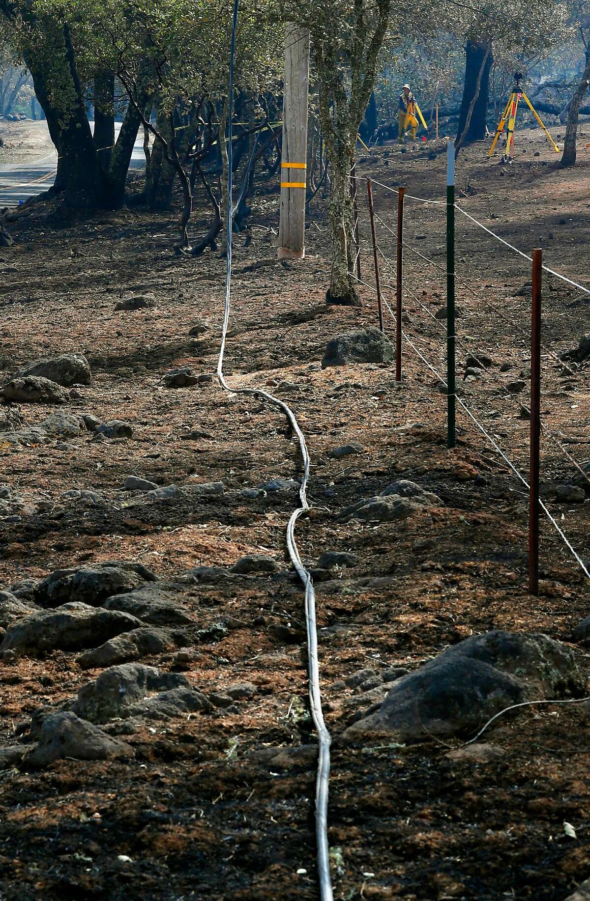 Burned power lines on the ground as investigators (background) searched for the cause of the Atlas fire east of Santa Rosa, Ca. as seen on Tuesday October 17, 2017.