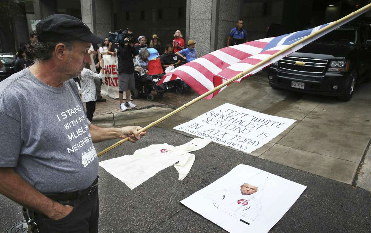 Reggie Fesenden walks by posters and a KKK gown placed in front of official cars as Attorney General Jeff Sessions talked before a group of law enforcement officials Friday.