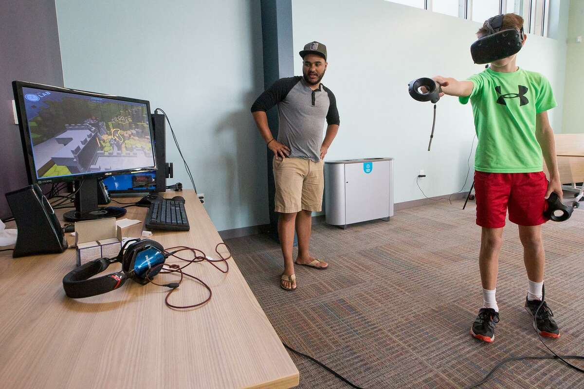 Nathaniel Shandersky (right), 12, uses wireless controllers and a HMB (head mounted display) to navigate inside a three-dimensional environment as Jason Flinn gives a virtual reality demonstration at the Universal City Library on Saturday, Oct. 21.