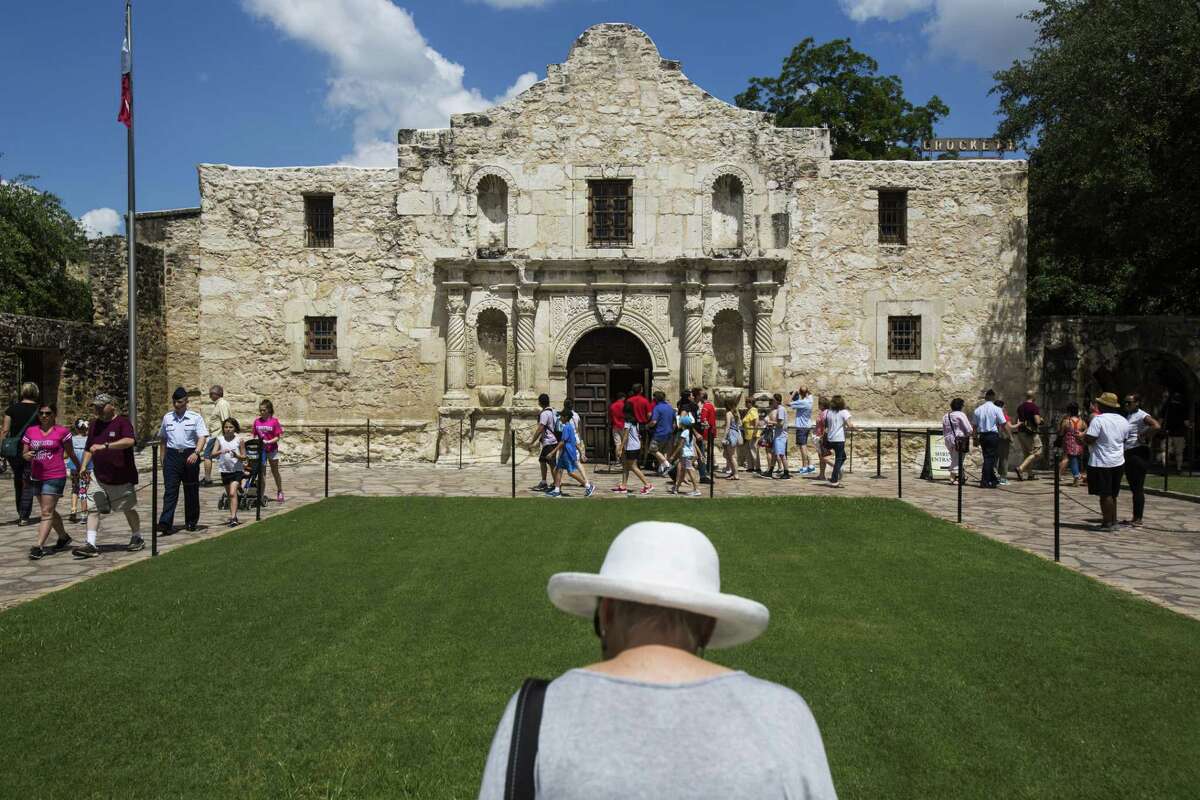 A woman reads a plaque in front of The Alamo as tourists make their entrance into the building on Friday, June 10, 2016.