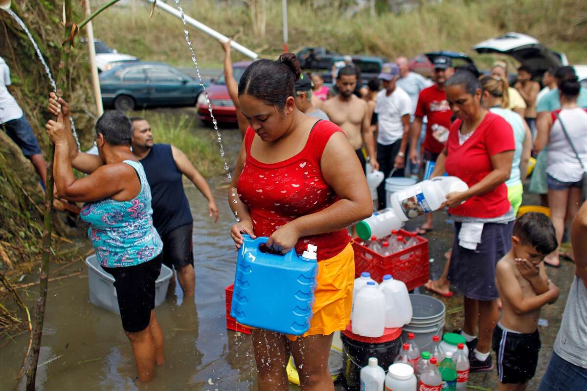 People collect water from a natural spring created by the landslides in a mountain next to a road in Corozal, west of San Juan.