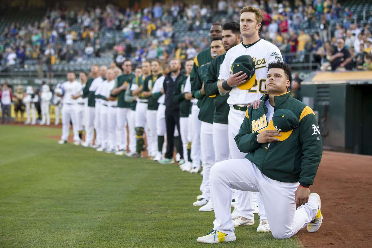 From right: Oakland Athletics catcher Bruce Maxwell (13) takes a knee as Oakland Athletics left fielder Mark Canha (20) puts his hand on his shoulder during the playing of the national anthem before an MLB baseball game between the Oakland Athletics and Texas Rangers at the Oakland Coliseum on Saturday, Sept. 23, 2017, in Oakland, Calif.