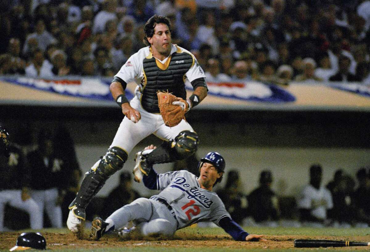 Oakland A's catcher Ron Hassey leaps out of the way of sliding Los Angeles Dodgers Danny Heep after making the sixth inning forceout on a ball hit by Jeff Hamilton. The Dodgers failed to score in the inning despite loading the bases with no outs in the third game of the World Series at Oakland Coliseum, Oct. 18, 1988. (AP Photo/Eric Risberg)