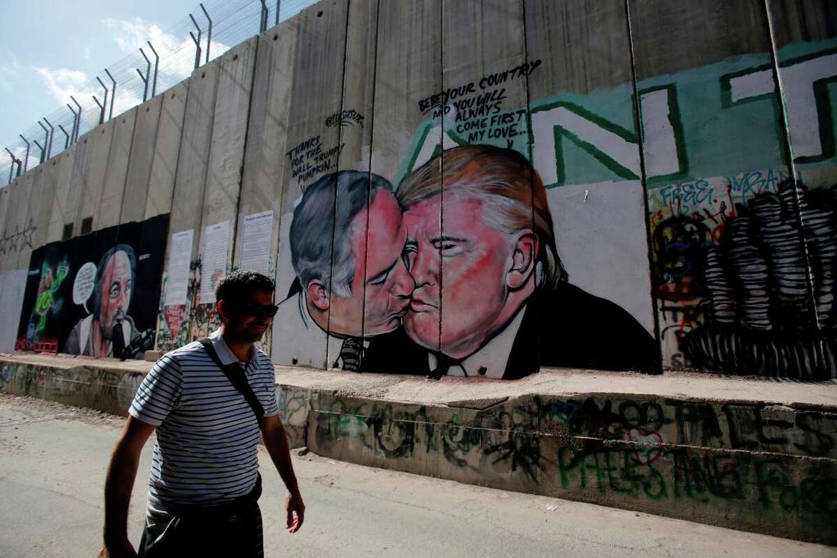 A tourist walks past a graffiti by street artist Lushsux, depicting US President Donald Trump kissing Israeli Prime Minister Benjamin Netanyahu drawn on the controversial Israeli separation barrier separating the West Bank town of Bethlehem from Jerusalem, on October 29, 2017. / AFP PHOTO / Musa AL SHAER (Photo credit should read MUSA AL SHAER/AFP/Getty Images)