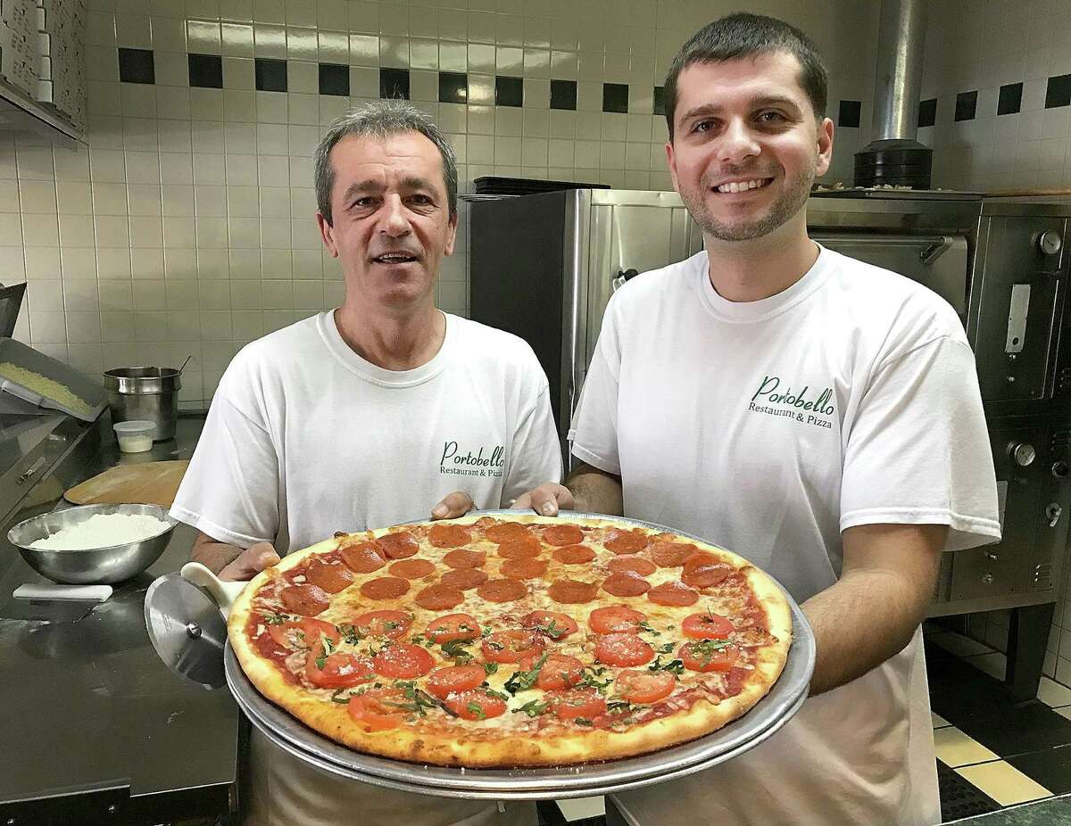 Kenny and Ilir Alka hold a half pepperoni, half tomato pizza at their restaurant, Portobello, in Brookfield, Conn., on Thursday, Nov. 2, 2017. Portobello is celebrating 20 years in business on Friday.