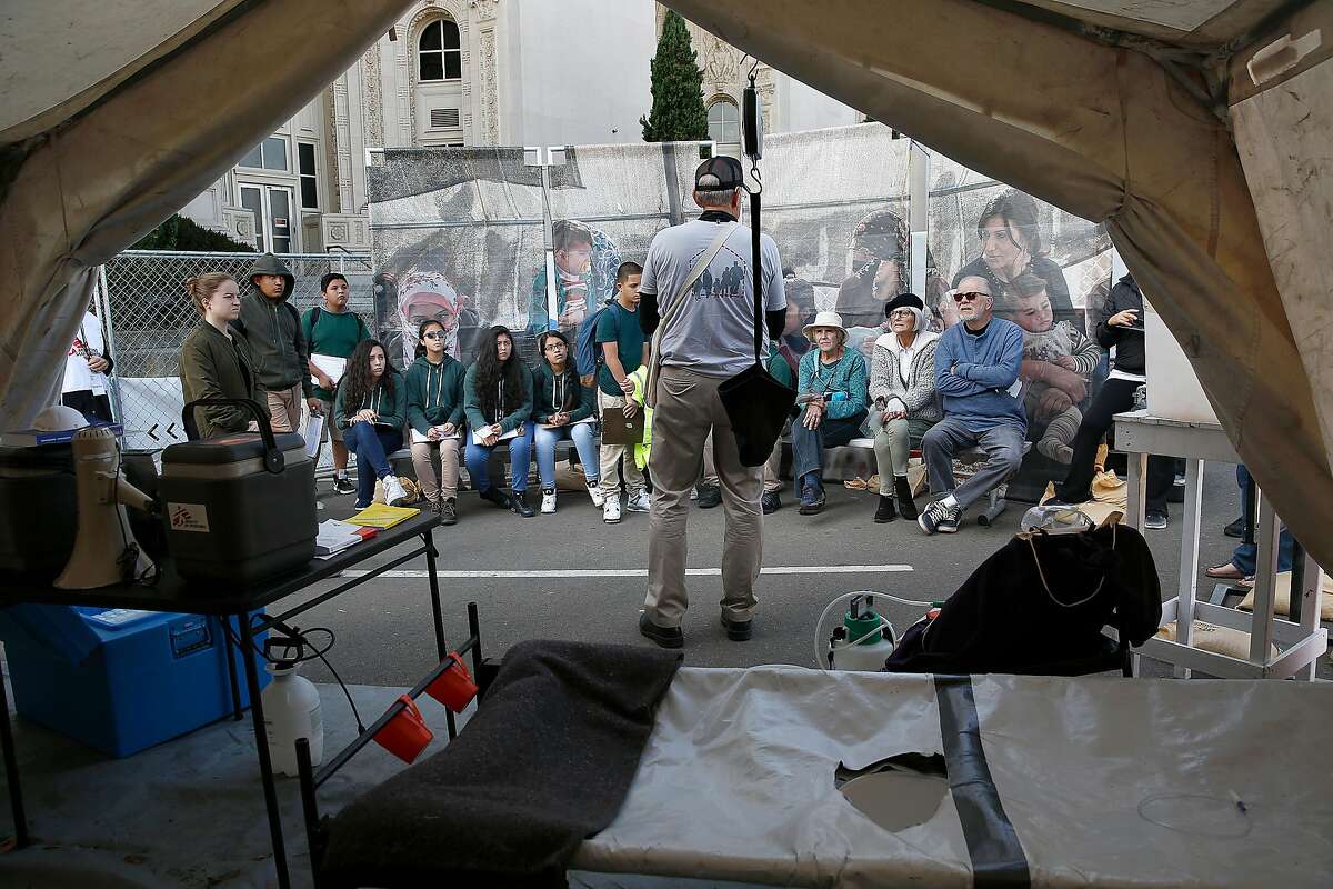 Tour guide Jim Peck (middle) gives students from Lighthouse Community Charter School and visitors a view of a tent Doctors Without Borders would use to treat refugee patients at "Forced From Home," an interactive outdoor exhibition about the global refugee crisis at the Henry J Kaiser Convention Center parking lot on Tuesday, October 31, 2017, in Oakland, Calif.