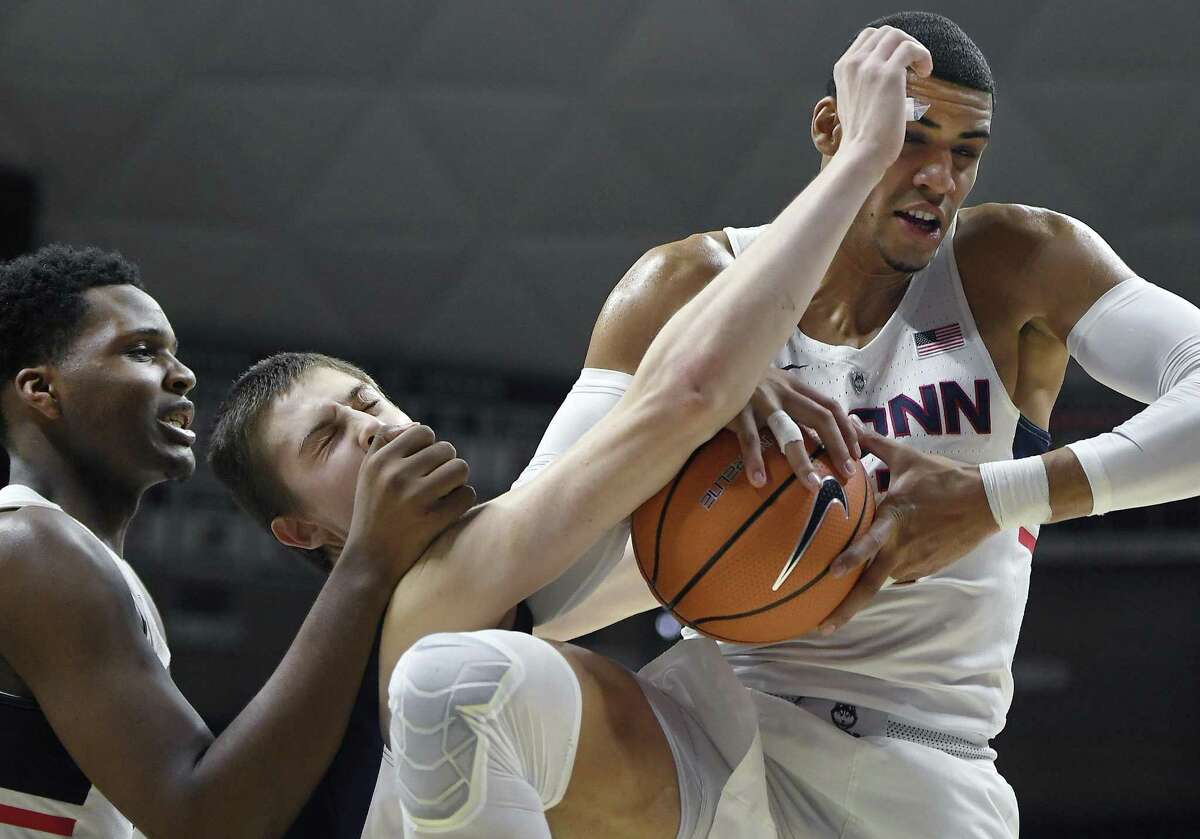 Queens College's Kevin Buron, center, is sandwiched between UConn’s Eric Cobb, left, and Kwintin Williams as Williams pulls down a rebound in the first half Sunday in Storrs.