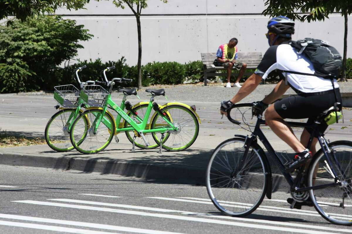 A Seattle bicyclist passes two LimeBike cycles in lower Queen Anne on July 26. LimeBike is one of six companies that offer dockless bike sharing considering launching in Houston.
