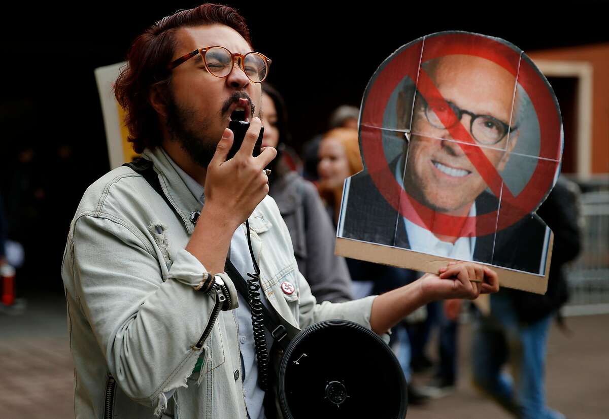 Justin Deckard, who holds a cardboard head of UC regent Norman Pattiz, protests outside the William J. Rutter Center as the Regents of the University of California meet inside, Wednesday, Nov. 15, 2017, in San Francisco, Calif. Demonstrators demanded the resignation of one of the regents, Norman Pattiz. Deckard comes from the UCSB student activist network.