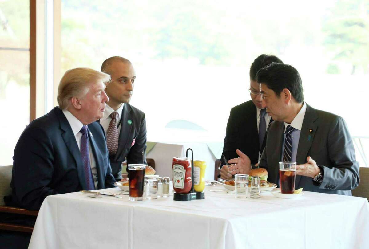 FILE - In this Nov. 5, 2017, file photo from the Prime Minister's Office Facebook page, U.S. President Donald Trump, left, listens to Japanese Prime Minister Shinzo Abe, right, during a lunch of hamburgers from Munch's Burger Shack at Kasumigaseki Country Club in Kawagoe, Japan. The cheeseburger Trump had is still drawing lines to the Tokyo burger joint. (Cabinet Public Relations Office of Japan via AP)