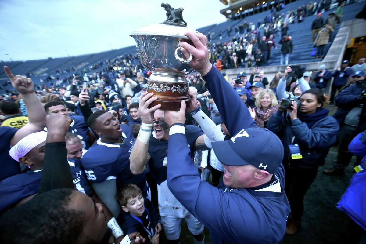 Spencer Rymiszewski (center) and Yale head coach Tony Reno hold the Ivy League Football Trophy after defeating Harvard 24-3 at the Yale Bowl in New Haven on November 17, 2017.