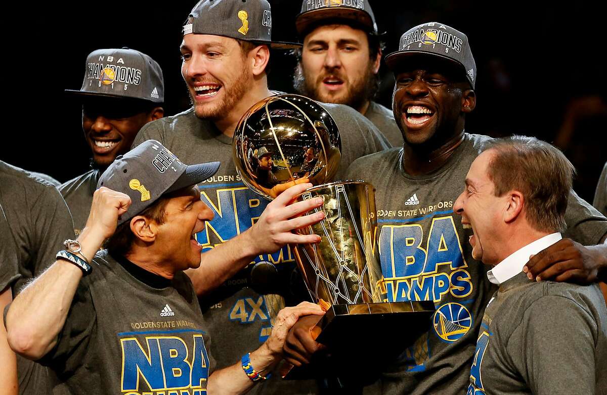 Draymond Green #23 David Lee #10 and Andrew Bogut #12 of the Golden State Warriors celebrates with team owners Peter Guber and Joe Lacob and the Larry O'Brien NBA Championship Trophy after defeating the Cleveland Cavaliers 105 to 97 to win Game Six of the 2015 NBA Finals at Quicken Loans Arena on June 16, 2015 in Cleveland, Ohio.