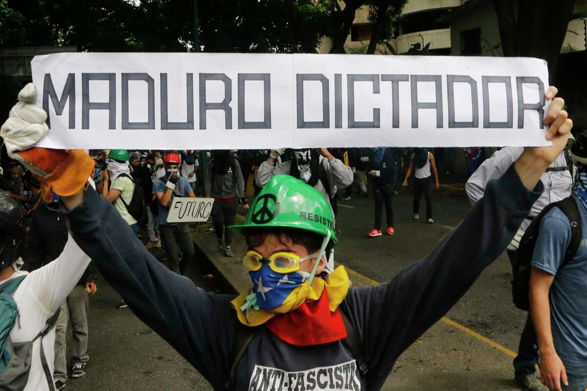 An opponent to President Nicolas Maduro holds a sign that reads in Spanish "Maduro dictator," referring to President Nicolas Maduro, at an opposition May Day march in Caracas, Venezuela, Monday, May 1, 2017. Venezuelans are taking to the streets in dueling anti- and pro-government May Day demonstrations as an intensifying protest movement enters its second month. (AP Photo/Ariana Cubillos)