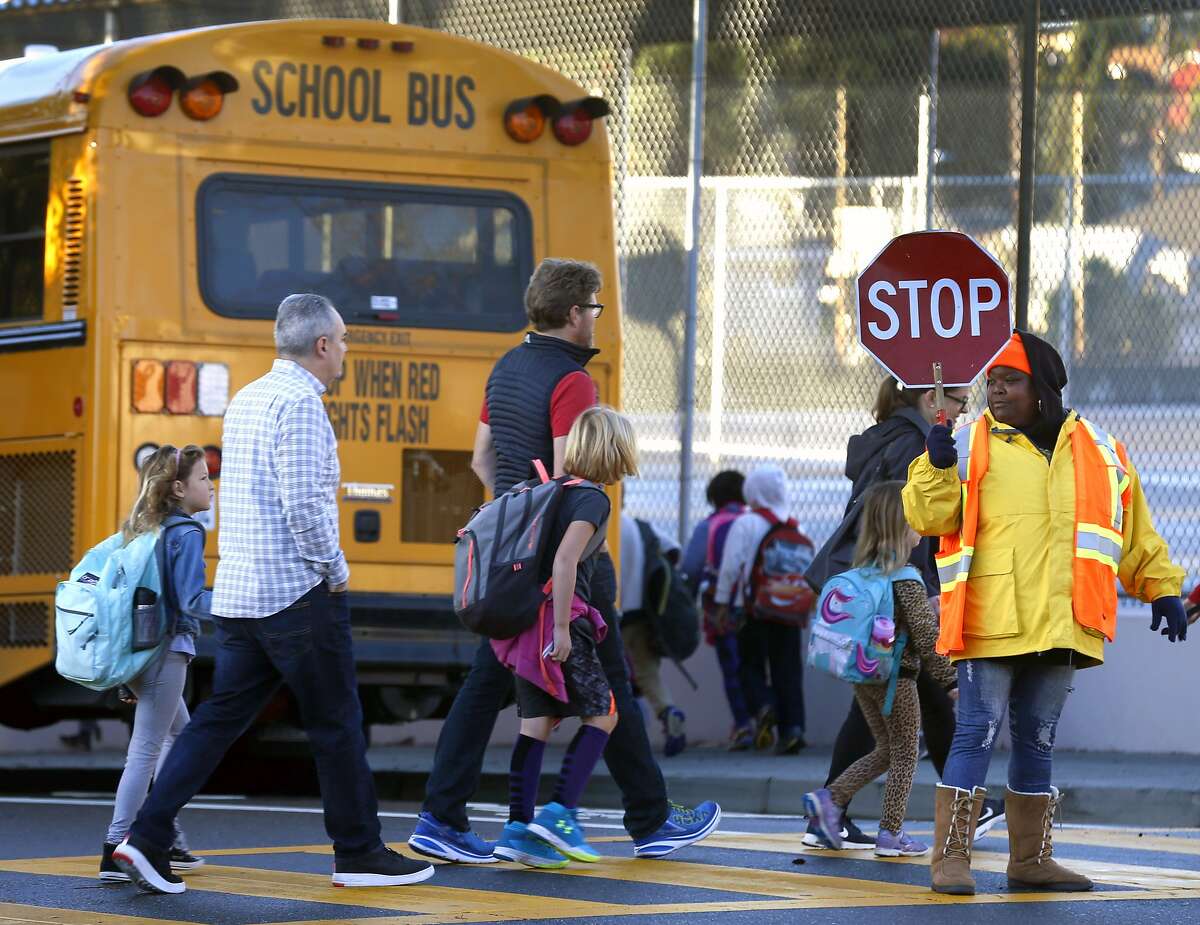 A crossing guard stops traffic for parents and Glenview Elementary School students walking to a bus staging area at East 38th and Beaumont avenues in Oakland, Calif. on Friday, Nov. 17, 2017. Students are being bused to Santa Fe Elementary in North Oakland during reconstruction of their school. Delays and increased costs in the reconstruction of Glenview Elementary have angered parents and residents.