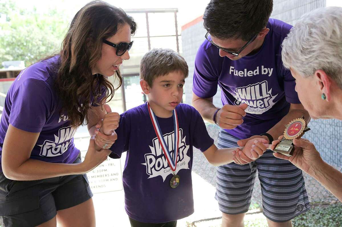 With his mom, Valerie, and dad, Tim, Will, 7, accepts an award from Roxanne Davis, community liaison for the YMCA in The Woodlands, for participating in a youth triathlon.