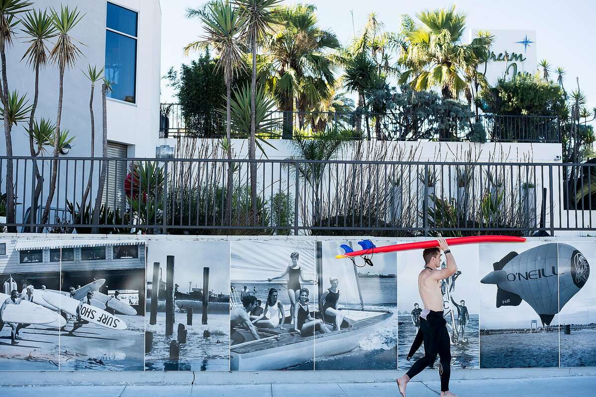 A surfer passes a mural of Jack O'Neill imagery outside the Dream Inn on Nov. 18, 2017 in Santa Cruz.