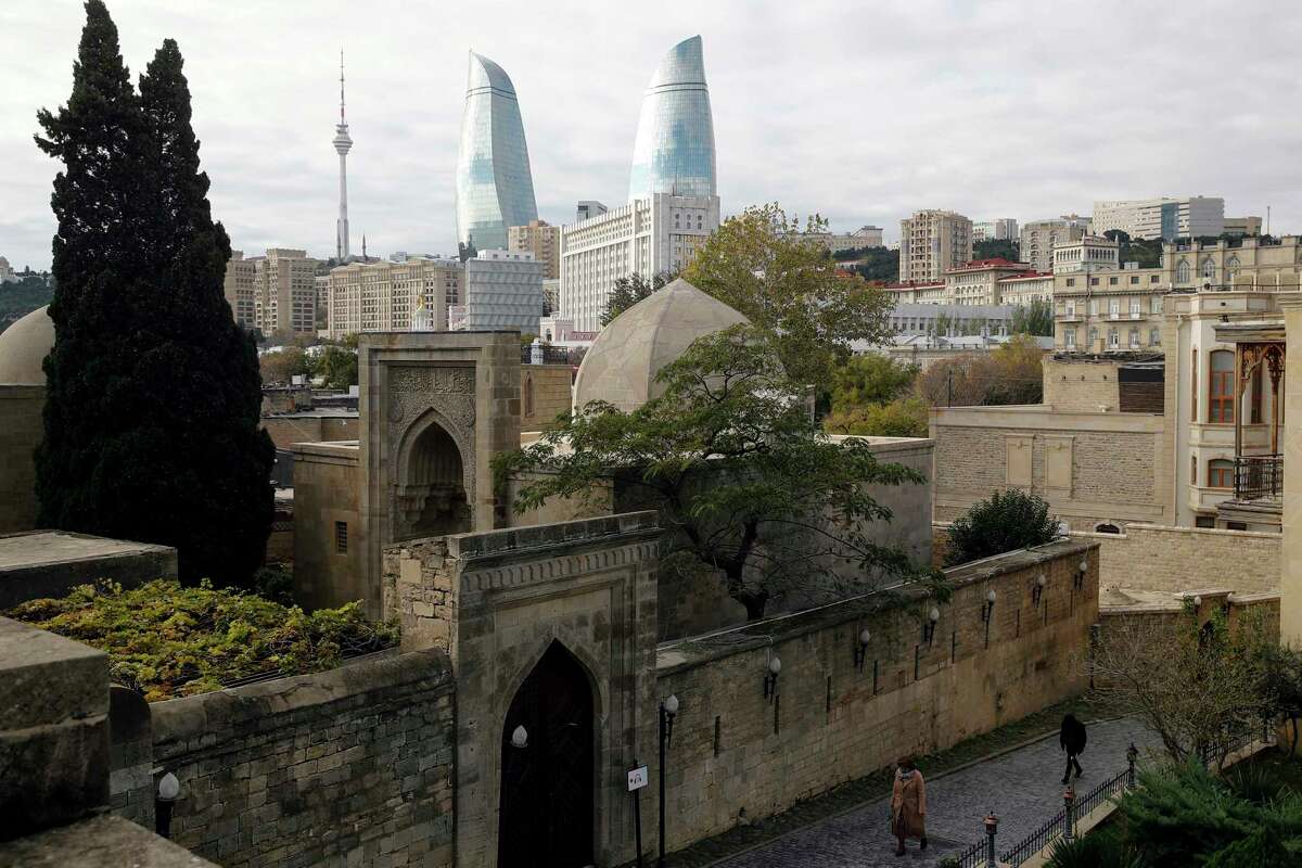 People walk in the Old City of Baku with the Flame Towers skyscrapers in background in Baku, Azerbaijan, on Nov. 23, 2017. (AP Photo/Pavel Golovkin)