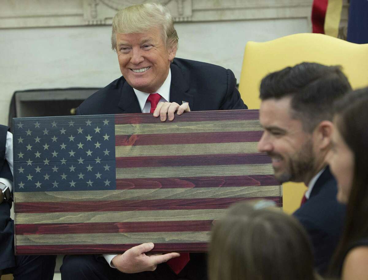 President Donald Trump holds an American flag plaque made by Brian Steorts, owner of Flags of Valor, during a meeting in the Oval Office Tuesday. Trump hosted four families from around the country to hear how tax reform could grow their businesses.(Bloomberg)