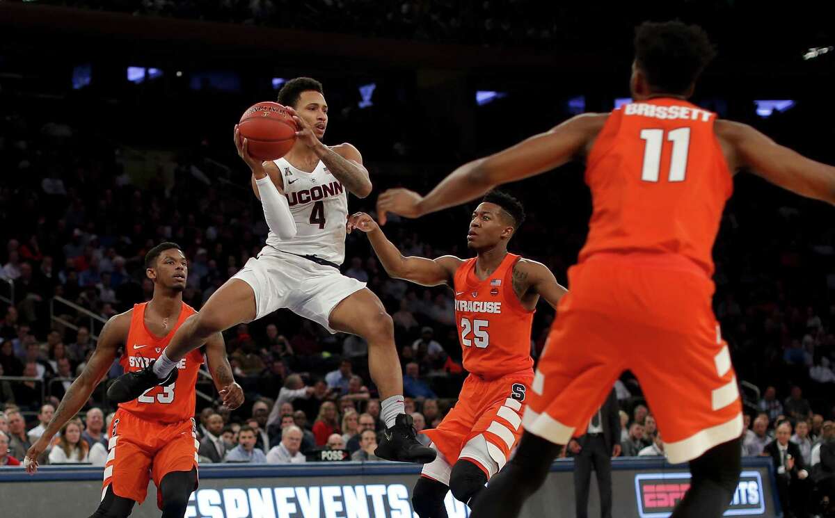 UConn guard Jalen Adams passes the ball off against Syracuse guard Tyus Battle (25), guard Frank Howard (23) and forward Oshae Brissett (11) during the first half on Tuesday.