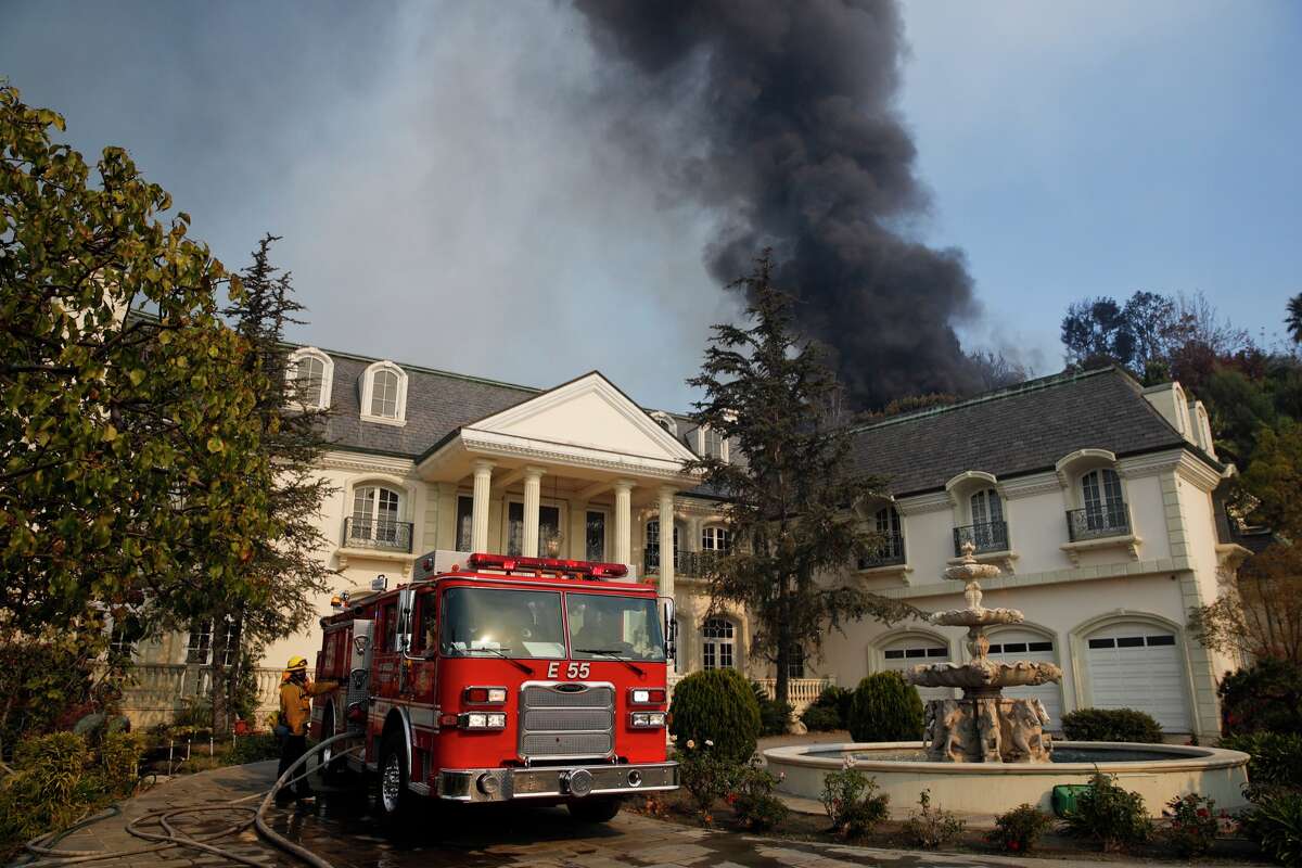A fire truck is parked outside a mansion as smoke from a wildfire rises behind the property, on Dec. 6, 2017, in the Bel-Air neighborhood of Los Angeles.