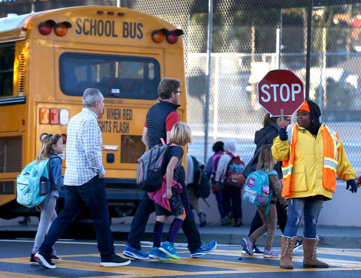 In this file photo, Oakland students walk across a street to board a bus.